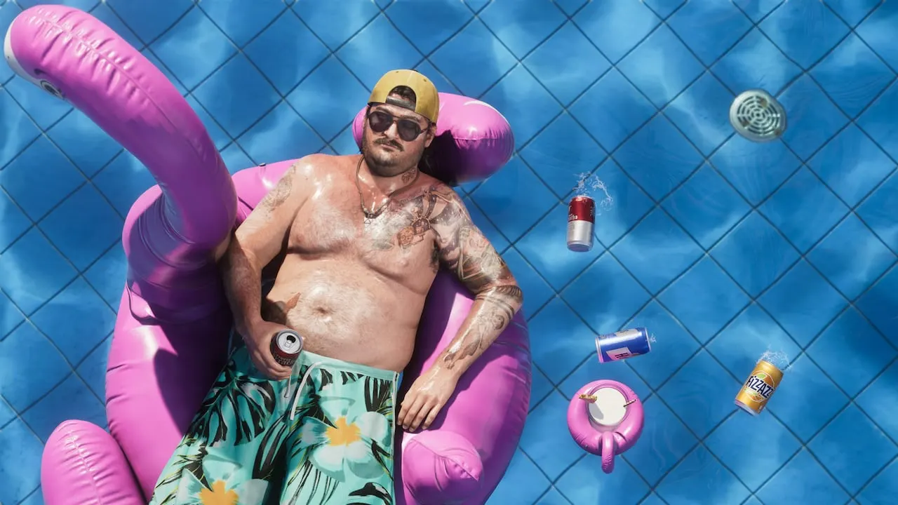 Cal Hampton in a cap and sunglasses, floating on a pink inflatable in a swimming pool